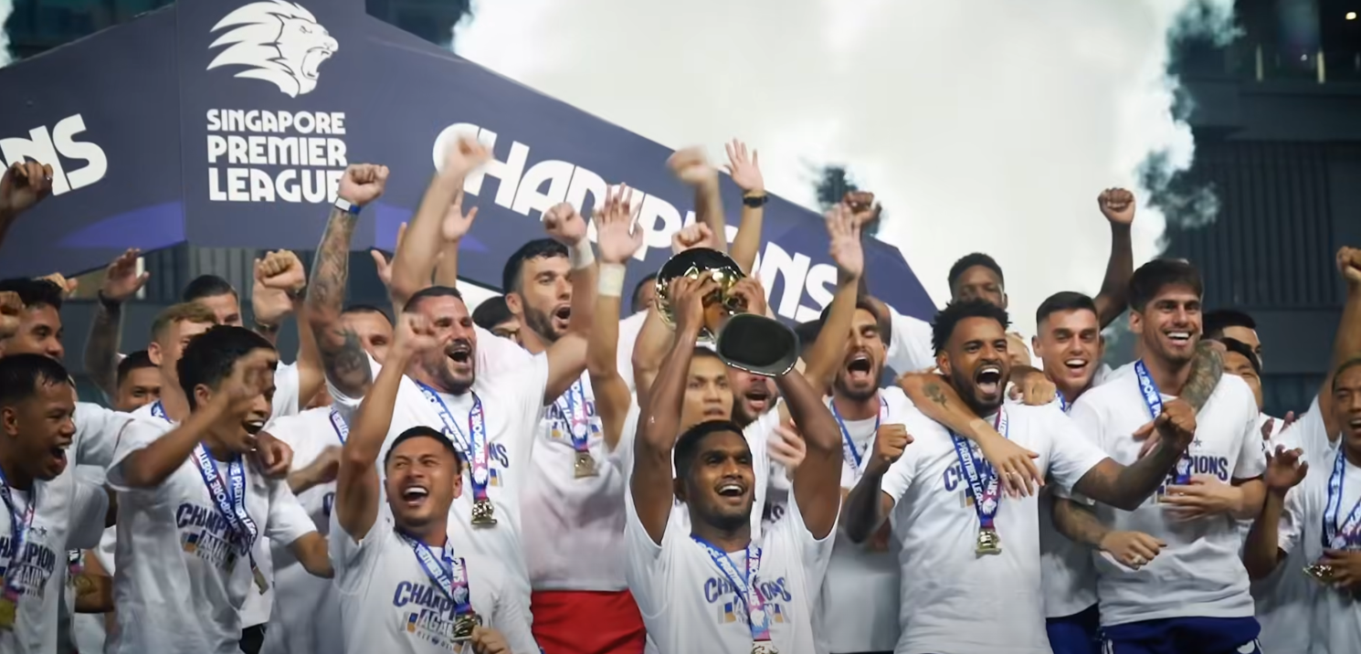 Singapore National Football Team players and coaching staff celebrating on the pitch while lifting a championship trophy